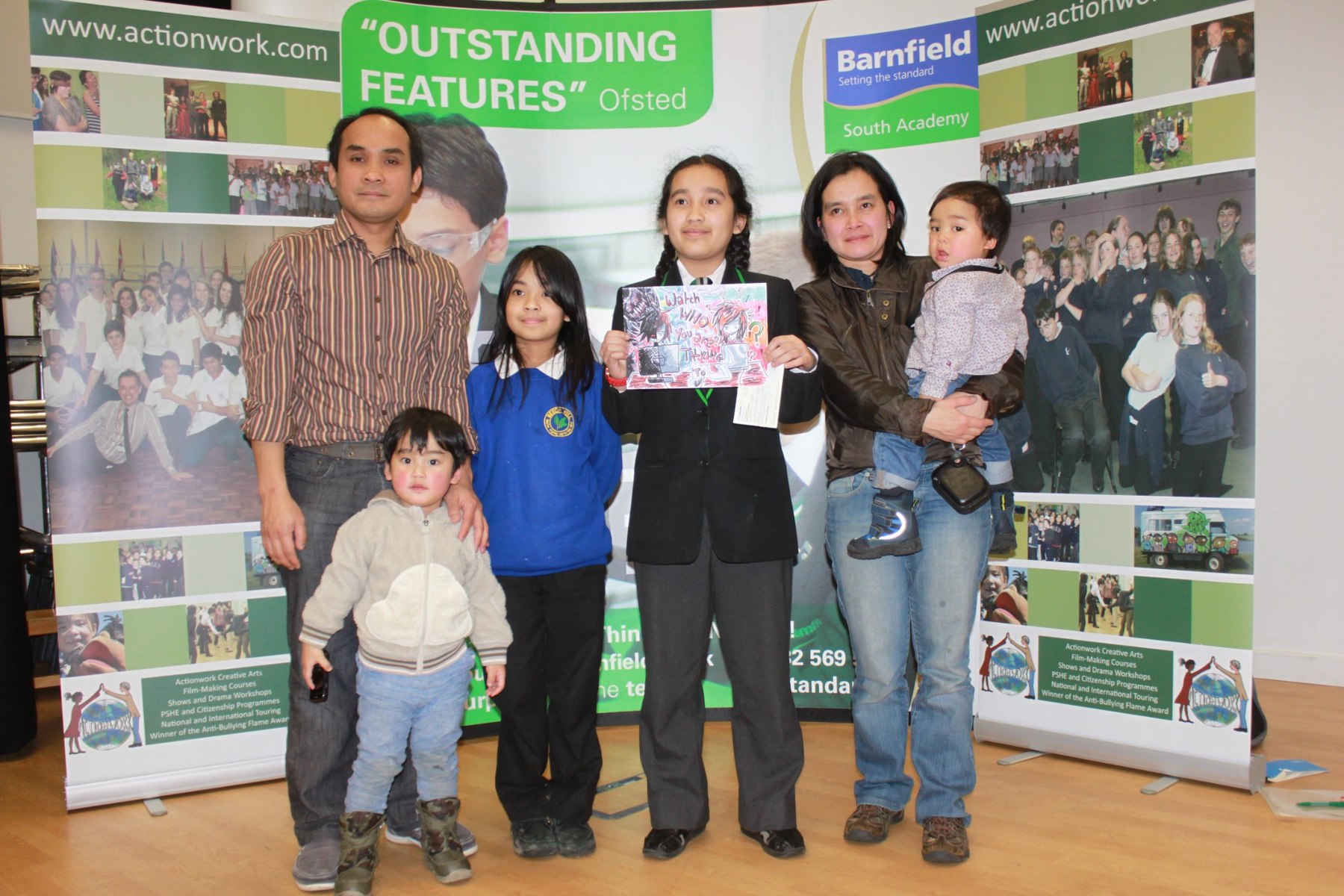 Young competition winner holding artwork during the 2013 Anti Bullying Week prize presentation, standing with other attendees